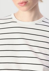 T-shirt a righe in cotone bianco con linee orizzontali nere, dotata di scollatura rotonda e texture morbida.