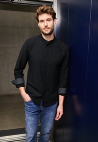Camicia nera con colletto alto, dotata di polsini grigi texturizzati, abbinata a jeans azzurri chiari. Tessuto liscio con una vestibilità su misura.