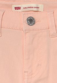 Różowe dżinsowe szorty girlfriend z przednią kieszenią, srebrnym guzikiem i widoczną metką "Levi's GIRLFRIEND SHORT" na pasku.