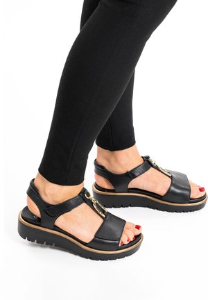 Black leather sandals with a thick platform sole and gold hardware accent. Open toe design, featuring straps and a side zipper.