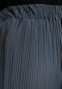 Tissu plissé gris foncé avec taille élastique froncée, montrant des plis verticaux et un détail tricoté texturé.