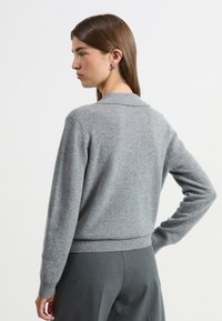 Szary, dzianinowy kardigan z kołnierzykiem i długimi rękawami. Posiada subtelną teksturę oraz dopasowaną talię. Gładki, lekki materiał.