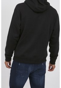 Sudadera negra con capucha ajustable, puños y dobladillo de canalé. Combinada con unos jeans oscuros, que tienen dos bolsillos traseros con un diseño sutil.