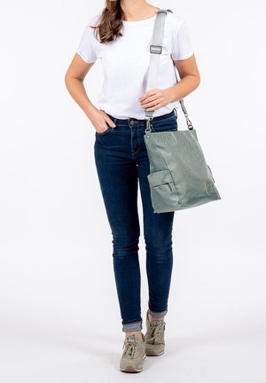 Groen schoudertas met patroon en een grijze riem, voorzien van twee voorzakken en een gladde textuur. Draagt een witte blouse en blauwe spijkerbroek.