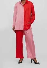 Zijden blouse en broek set, half rood en half roze, met een knoopsysteem kraag. Losse pasvorm en zachte textuur, gecombineerd met zwarte puntige hakken.