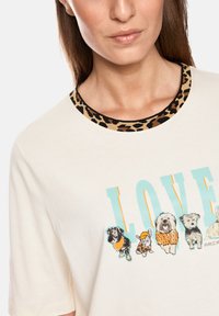 Cream-colored t-shirt featuring a leopard print neckline and colorful graphic with cartoon dogs and the word "LOVE" in bold letters.