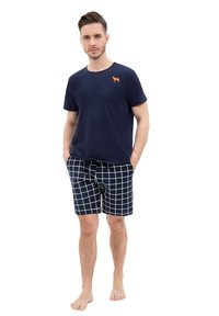 Marynarska koszulka z pomarańczowym logo psa, zestawiona z marynarskimi szortami z białym wzorem w kratę. Oba elementy mają luźny krój i miękką teksturę.