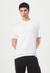 Witte katoenen t-shirt met een ronde halslijn en korte mouwen, met een ontspannen pasvorm en een soepele textuur, gecombineerd met zwarte broeken.
