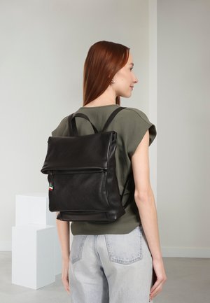 Zwarte leren rugzak met een textuur oppervlak, voorzien van een overslagklep en verstelbare riemen. Inclusief een klein gekleurd label.