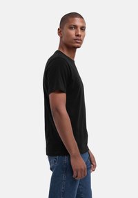 Schwarzes Baumwoll-T-Shirt mit einem klassischen Rundhalsausschnitt und kurzen Ärmeln, im Slim Fit. Getragen mit blauen Jeans.