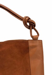 Sac à main en cuir marron avec un panneau avant en daim et un détail en cuir noué, sur fond blanc.