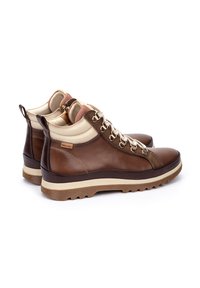Bottines en cuir marron avec des accents crème, des lacets texturés et une semelle en caoutchouc épaisse et à motifs. Comprend un logo sur le talon.