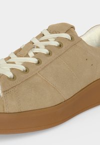 Baskets en daim beige avec lacets blancs et semelle en caoutchouc marron, présentées en gros plan sur fond blanc.