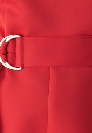 Rdeča tkaninska obleka z širokim pasom in srebrnim okroglim sponko ter lepimi gubami za teksturo in strukturo. Gladka površinska obdelava.