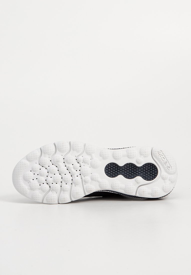 Chaussure de sport noire avec une semelle en caoutchouc blanc texturé présentant des motifs ronds variés et des trous de ventilation, conçue pour la respirabilité et le confort.