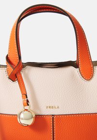 Torbica od narančaste i krem kože s dvostrukim ručkama, teksturiranom površinom, zlatnim detaljima i kontrastnim šavovima. Zlato "Furla" logo prikazan.