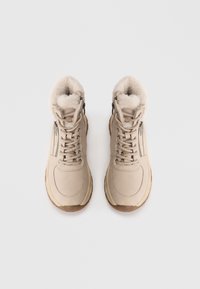 Beige høj-anførere med blødt pelsfor, der har en glat overflade, polstret krave og sidelukke for nem adgang.