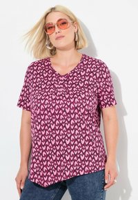 Korte mouw top in het roze met een hartjespatroon, voorzien van een V-halslijn en een licht gebogen zoom. Gepaard met blauwe denim jeans.