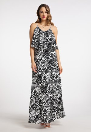 Frau trägt ein ärmelloses schwarz-weißes Zebra-Maxi-Kleid mit geschichtetem Oberteil und dünnen Trägern, steht vor einem einfarbigen hellen Hintergrund.