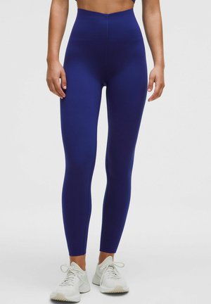 Navy blue high-waisted leggings made of stretchy fabric, featuring a smooth texture and fitted design, paired with white athletic shoes.