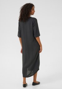 Robe maxi noire, ample, avec des manches courtes, longueur mi-mollet, en tissu doux et texturé. Présente une coupe droite et des fentes sur les côtés.