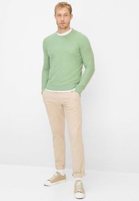 Groene trui met lange mouwen en ronde hals, gecombineerd met beige chino's en crème lage sneakers. Eenvoudig, met textuur.