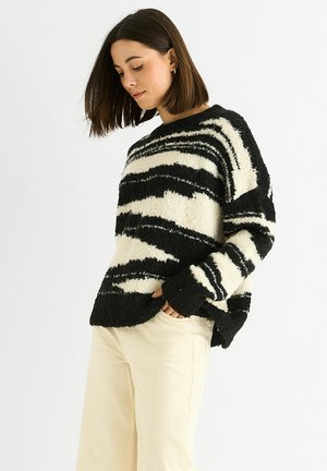 Black and white striped sweater made of fuzzy material. Features a crew neckline and long sleeves with wide cuffs. Worn over light-colored pants.