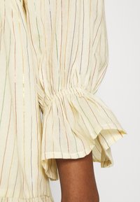 Blusa in lino crema con strisce verticali multicolori. Presenta maniche arricciate e bordo a peplo. Texture morbida con una leggera lucentezza.