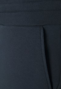 Mörkblå mjukisbyxor har en ribbad midja och en jämn yta med sidofickor, designade för komfort och rörelsefrihet.