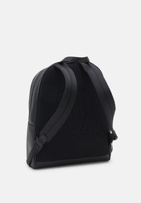 Zaino nero con schienale in mesh testurizzato, spallacci regolabili e pannello frontale liscio con un grande logo in rilievo.