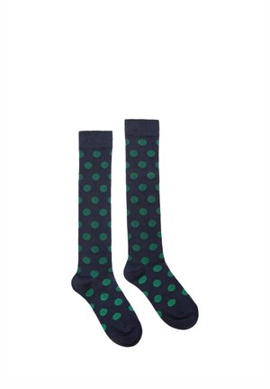 Paire de chaussettes montantes bleu marine avec des pois verts uniformément espacés, posées à plat sur un fond blanc.
