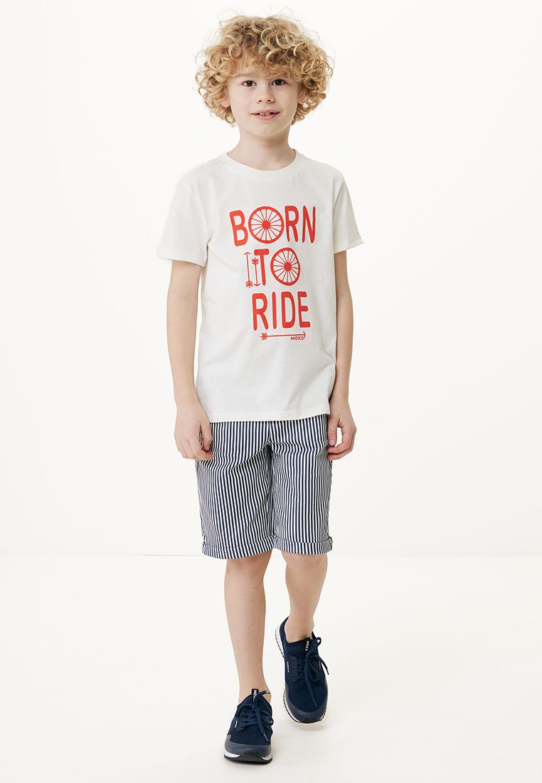 Biała koszulka z czerwonym napisem "BORN TO RIDE", zestawiona z niebiesko-białymi pasiastymi szortami. Ubrana w granatowe tenisówki. Dziecko stoi na jednolitym tle.