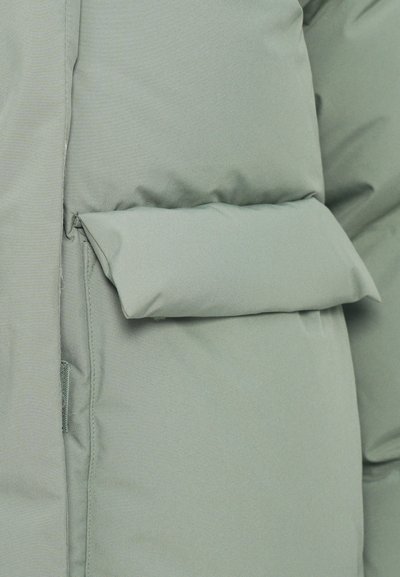 Padded green jacket with a smooth texture, featuring a prominent, flat pocket on the front. Stitching is visible along the seams.