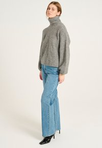 Pull à col roulé en tricot gris avec une texture côtelée, associé à un jean flare taille haute bleu clair et des chaussures à talons noires.