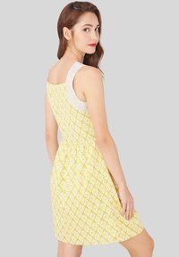 Vestido amarillo con patrón de diamantes blancos, tirante texturizado, cintura ajustada y falda acampanada. Tejido ligero con un diseño veraniego.