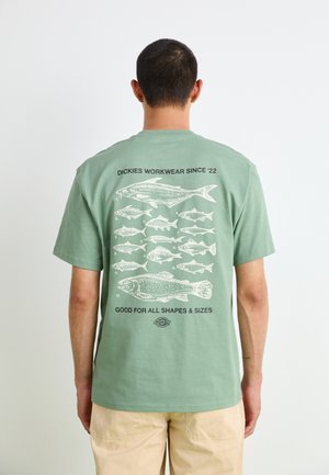 T-shirt vert clair à manches courtes avec une illustration de poisson et un texte au dos. Tissu en coton doux avec une coupe décontractée.