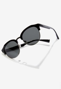 Ochelari de soare negri cu lentile circulare întunecate, ramă din plastic, accente argintii și un design distinctiv cu o formă superioară unică.