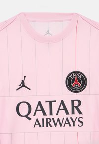 Ροζ φανέλα ποδοσφαίρου της Παρί Σεν Ζερμέν με λεπτές κάθετες ρίγες, λογότυπο Jumpman αριστερά, έμβλημα του συλλόγου δεξιά και κείμενο χορηγού Qatar Airways.