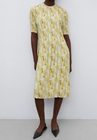 Žluté šaty do kolen s abstraktními vzory v odstínech žluté a šedé; vyrobené z skladané tkaniny; kulatý výstřih, krátké rukávy.