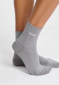Calcetines de tobillo grises con textura de canalé y acentos de purpurina, con la palabra "BARE" bordada en blanco en el lateral.