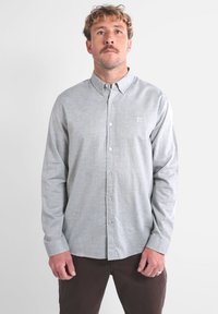 Chemise grise à boutons en tissu léger avec une texture subtile et un petit logo brodé sur la poitrine. Manches longues et col standard.