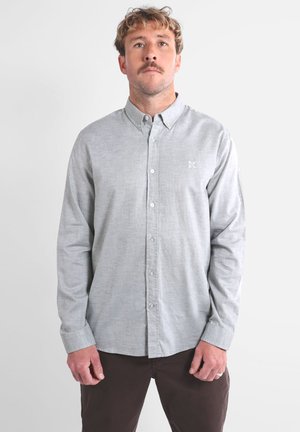 Chemise grise à boutons en tissu léger avec une texture subtile et un petit logo brodé sur la poitrine. Manches longues et col standard.