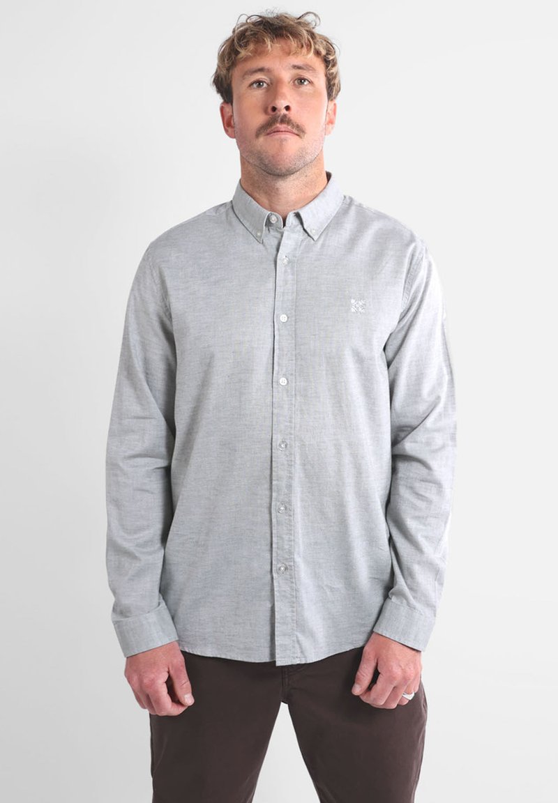 Chemise grise à boutons en tissu léger avec une texture subtile et un petit logo brodé sur la poitrine. Manches longues et col standard.