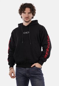 Felpa nera con cappuccio, logo frontale e grafiche rosse sulle maniche, dotata di lacci e vestibilità ampia, realizzata in tessuto morbido.
