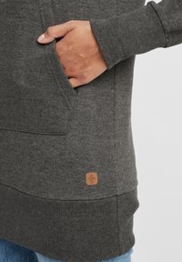 Mörkgrå sweatshirt med en kenguruficka, ribbade ärmslut och en fyrkantig läderetikett i nederkant till vänster. Mjuk, strukturerad tyg.