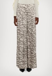 Pantalons large en motif camouflage beige et gris, avec des plis et une finition en tissu lisse, dotés d'un classique bouton de fermeture.