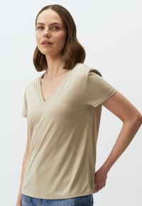 Beżowa koszulka typu V-neck wykonana z miękkiego materiału, z krótkimi rękawami i dopasowanym krojem. Gładka tekstura z minimalnymi przeszyciami na szwach.