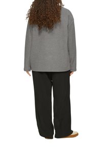 Grauer übergroßer Sweatshirt mit langen Ärmeln, lockere schwarze Hose und hellfarbige Schuhe. Der Stoff wirkt weich und hat eine entspannte Passform.
