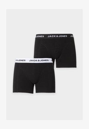 Õhuke tumedanahaline mees seisab paljajalu, seljas mustad Jack & Jones bokserid, taustaks hele ja ühtlane valgus, vaade küljele.