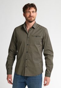 Langarmshirt van een gemusterd stof met blauw, beige en zwarte tinten, voorzien van een knoopsluiting aan de voorkant en een borstzak.